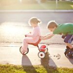 siblings payings girl kid riding cycle while boy pushing